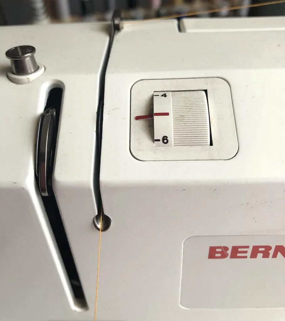 Creating tension on the upper thread by guiding thread through tension discs on the Bernina sewing machine