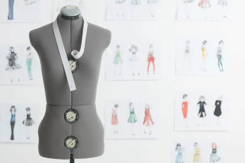 Grey adjustable dress form with fashion sketches on wall behind.