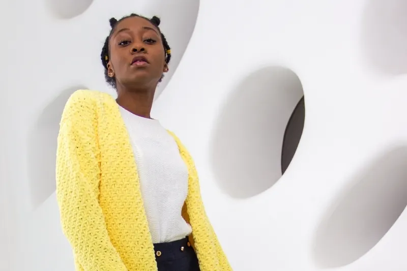 A yellow long cardigan type of sweater worn by a young black woman