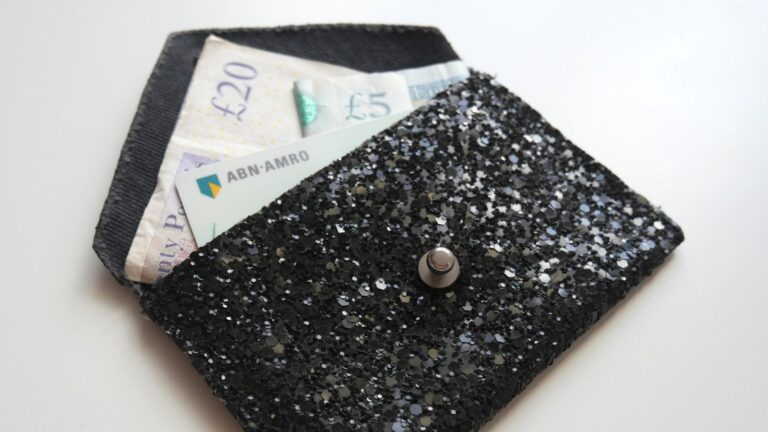 A small purse made from black encrusted denim, with British bank notes visible