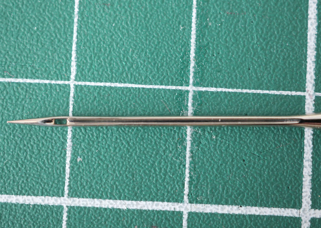The long groove on a sewing machine needle runs the length of the needle from the shank to the eye, but on one side only.