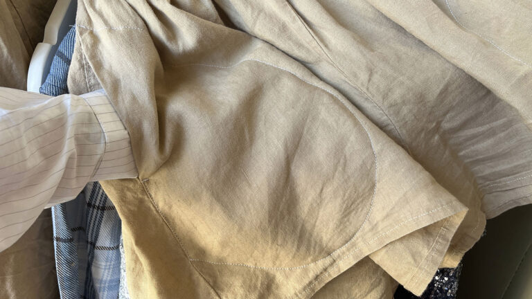 A hand inserted into a pocket that has been topstitched into place on linen shorts.