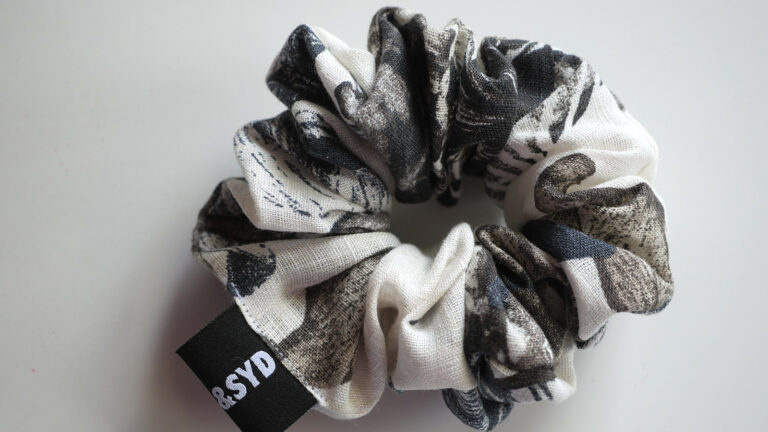 An abstract floral scrunchie in charcoal, blue and off white on a white table