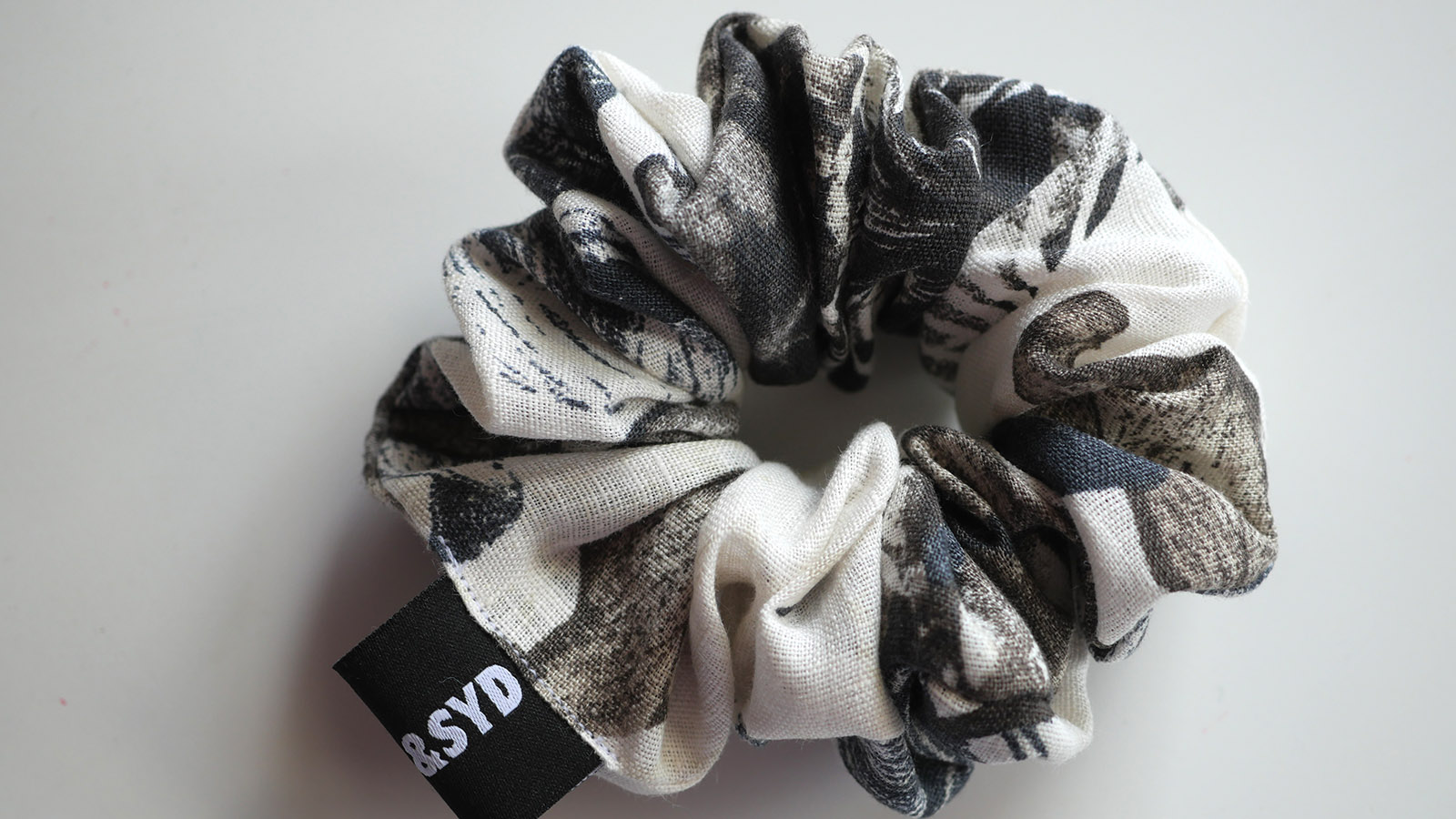 An abstract floral scrunchie in charcoal, blue and off white on a white table